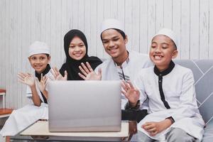 gelukkige moslimfamilie doet videogesprek vooraan een laptop met hallo of groet gebaar met de hand op eid mubarak-viering foto