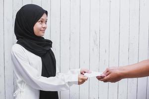 jonge moslimvrouw die een witte envelop geeft om thr te geven of zakat fitrah te betalen als een verplichting in de heilige maand ramadan foto