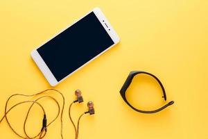 fitnessconcept met mobiele telefoon, oortelefoons en fitnesstracker op gele achtergrond foto