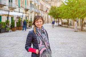 jonge mooie vrouw reiziger met zwarte jas camera kijken, glimlachen en poseren in het historische centrum van de stad Matra foto