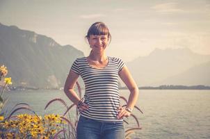 jong mooi meisje met gestreept shirt en spijkerbroek poseren en glimlachen aan de oever van het meer van Genève foto