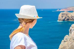 jonge vrouw reiziger met witte hoed en shirt verblijft in cabo de sao vicente cape saint vincent foto