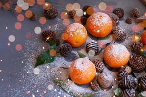 oranje mandarijnen op grijze achtergrond in nieuwjaarsdecor met bruine dennenappels en groene bladeren. kerstversiering met mandarijnen. heerlijke zoete clementine. foto