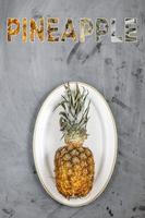 witte plaat met rijpe hele ananas op grijze betonnen ondergrond. woord ananas. foto