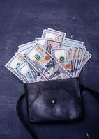dollars in een zwarte leren tas op een zwarte cementachtergrond. financieel en zakelijk concept. foto