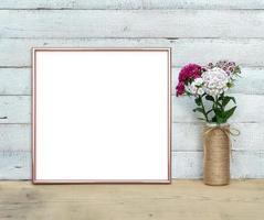 rose gouden vierkante frame mockup in de buurt van een boeket van zoete william staat op een houten tafel op een geschilderde witte houten achtergrond. rustieke stijl, eenvoudige schoonheid. 3D render. foto