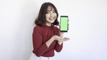 gelukkig Aziatisch mooi meisje wijst op groen scherm telefoon op witte achtergrond foto