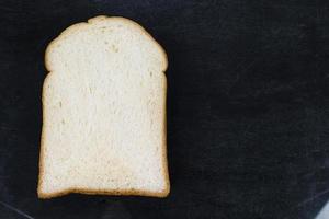 Witte sneetje brood geïsoleerd op zwarte houten achtergrond foto