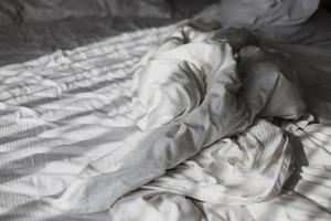 rommelige deken op het bed met zonlichtschaduwen in de ochtend foto