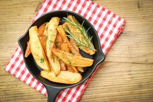Aardappelpartjes op bord met rozemarijnkruid, frietjes koken of aardappelen bakken - bovenaanzicht foto