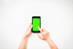 vrouwelijke hand toont mobiele smartphone met groen scherm in verticale positie geïsoleerd op een witte achtergrond met vinger tik scherm. mock-up advertentieconcept voor mobiele technologie. foto