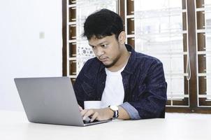 jonge aziatische man die zich serieus voelt als een laptop op tafel werkt. foto