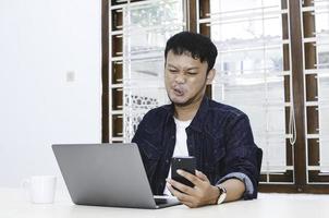 jonge aziatische man voelt zich verdrietig wanneer werklaptop en telefoon op tafel liggen. foto