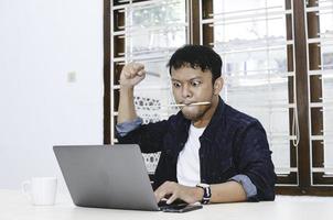 jonge aziatische man die zich serieus voelt als een laptop op tafel werkt. foto