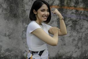 prachtige sterke jonge aziatische vrouw met een whute-shirt met biceps en glimlachen. Indonesisch meisje sterk concept. foto