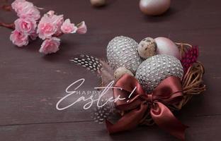 inscriptie vrolijk pasen nest met eieren op een houten achtergrond. vrolijk pasen-wenskaart met creatieve paaseieren en bloesembloemen foto