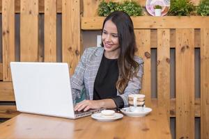 glimlachende vrouw die op laptop typt en koffie en dessert drinkt foto