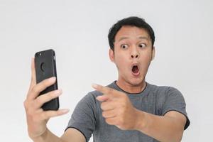 wow gezicht van je aziatische man geschokt door wat hij ziet in de smartphone op geïsoleerde grijze achtergrond. foto