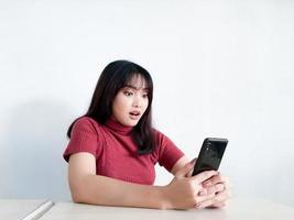 Aziatisch mooi meisje is geschokt in de smartphone op de geïsoleerde witte achtergrond foto