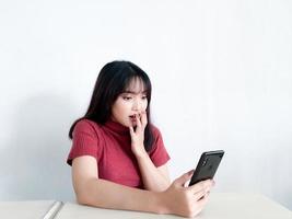 Aziatisch mooi meisje is geschokt in de smartphone op de geïsoleerde witte achtergrond foto