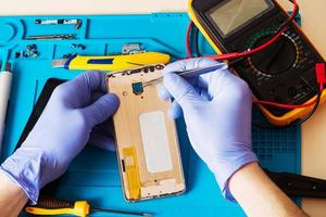 vakman in rubberen handschoenen repareert of onderhoudt een mobiele telefoon op een speciale rubberen mat voor reparatie. uitzicht van binnen foto