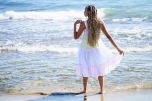 zwarte vrouw die langs de kust van het strand loopt en een mooie lange jurk draagt. foto