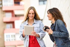 twee jonge toeristische vrouwen op zoek naar kaarten met digitale tablet buitenshuis. foto