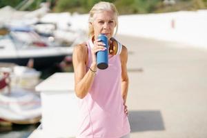 volwassen sportvrouw in fitnesskleding drinkwater uit een metalen fitnessfles buitenshuis.
