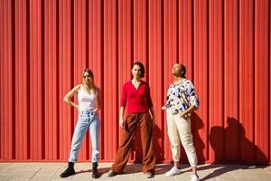 stijlvolle jonge diverse dames die tegen een rood hek op straat staan foto