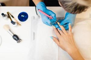 close-up van schoonheidsspecialiste die de nagels van haar cliënt schildert in blauwe en gele nagellak. foto