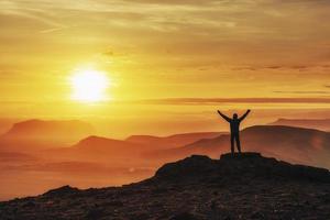 gelukkige man die bij zonsondergang op een klif staat foto