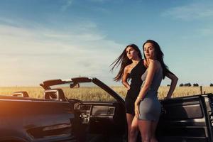 twee sexy brunette vrouw staande in de buurt van haar auto foto
