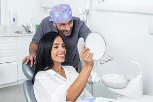 tandarts en cliënt kijken de tanden van de cliënt in de spiegel in een kliniek foto