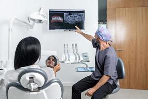 tandarts die een röntgenfoto laat zien aan een patet die op een stoel in een kliniek zit foto