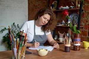 artisanale vrouw die n notitieboekje schrijft, dag in dagboek plant. mooie zakelijke vrouwelijke ondernemer foto