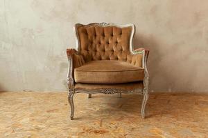 mooie luxe klassieke biege schone binnenkamer in grunge-stijl met bruine barokke fauteuil. vintage antieke bruin-grijze stoel die naast de muur staat. minimalistisch huisontwerp.