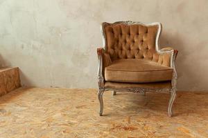 mooie luxe klassieke biege schone binnenkamer in grunge-stijl met bruine barokke fauteuil. vintage antieke bruin-grijze stoel die naast de muur staat. minimalistisch huisontwerp. foto