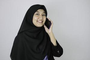 glimlachende jonge aziatische islamvrouw die een hoofddoek draagt, glimlacht als ze aan het bellen is foto