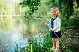 schattig klein blond meisje is tegen de achtergrond van water en g foto