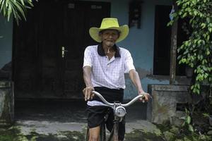 een portret van een Indonesische oude boer draagt een gele hoed met een oude fiets foto