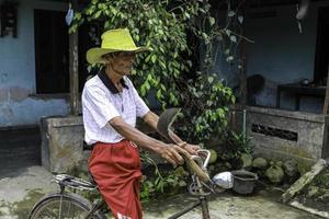 een portret van een Indonesische oude boer draagt een gele hoed met een oude fiets foto