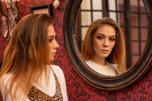 portret van een mooie jonge vrouw die bij de spiegel staat en naar zijn spiegelbeeld kijkt foto