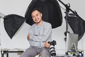 Aziatische fotograaf zit en houdt de camera vast met een zelfverzekerde glimlach foto