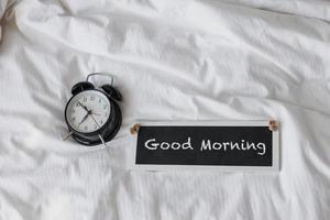 zwarte wekker op het bed met bord voor goedemorgen foto