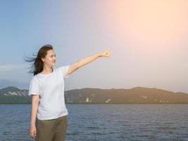 Aziatisch meisje in wit overhemd gebruik je vingers om naar de lucht te wijzen als een bedoeld doelwit. ze ziet er gelukkig uit daag de wind uit naar de zee en de zon op de dag dat ze op vakantie kwam foto