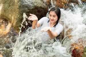 Aziatische vrouw die bij een waterval rondhangt. ze wil plezier hebben op vakantie. de waterval is erg koud omdat het natuurlijk water is. foto