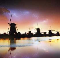 bliksem in bewolkte donkere hemel. traditionele Nederlandse windmolens kanaal foto