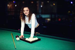 jong krullend meisje poseerde in de buurt van biljarttafel. sexy model bij zwarte mini minirok spelen russisch snooker. speel spel en leuk concept. foto