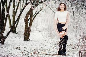 krullend brunette meisje achtergrond vallende sneeuw, draag op warme gebreide trui, zwarte minirok en wollen kousen. model op de winter. mode portret bij besneeuwd weer. instagram getinte foto. foto