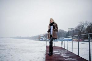 portret van jonge elegantie blond meisje in een bontjas op pier achtergrond mistige rivier op winterijs. foto
